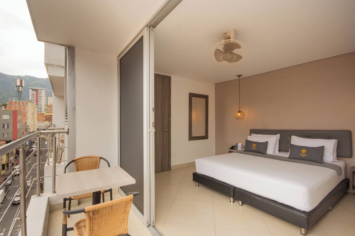Quarto de hotel com varanda, cama com roupa de cama branca e vista para a cidade.