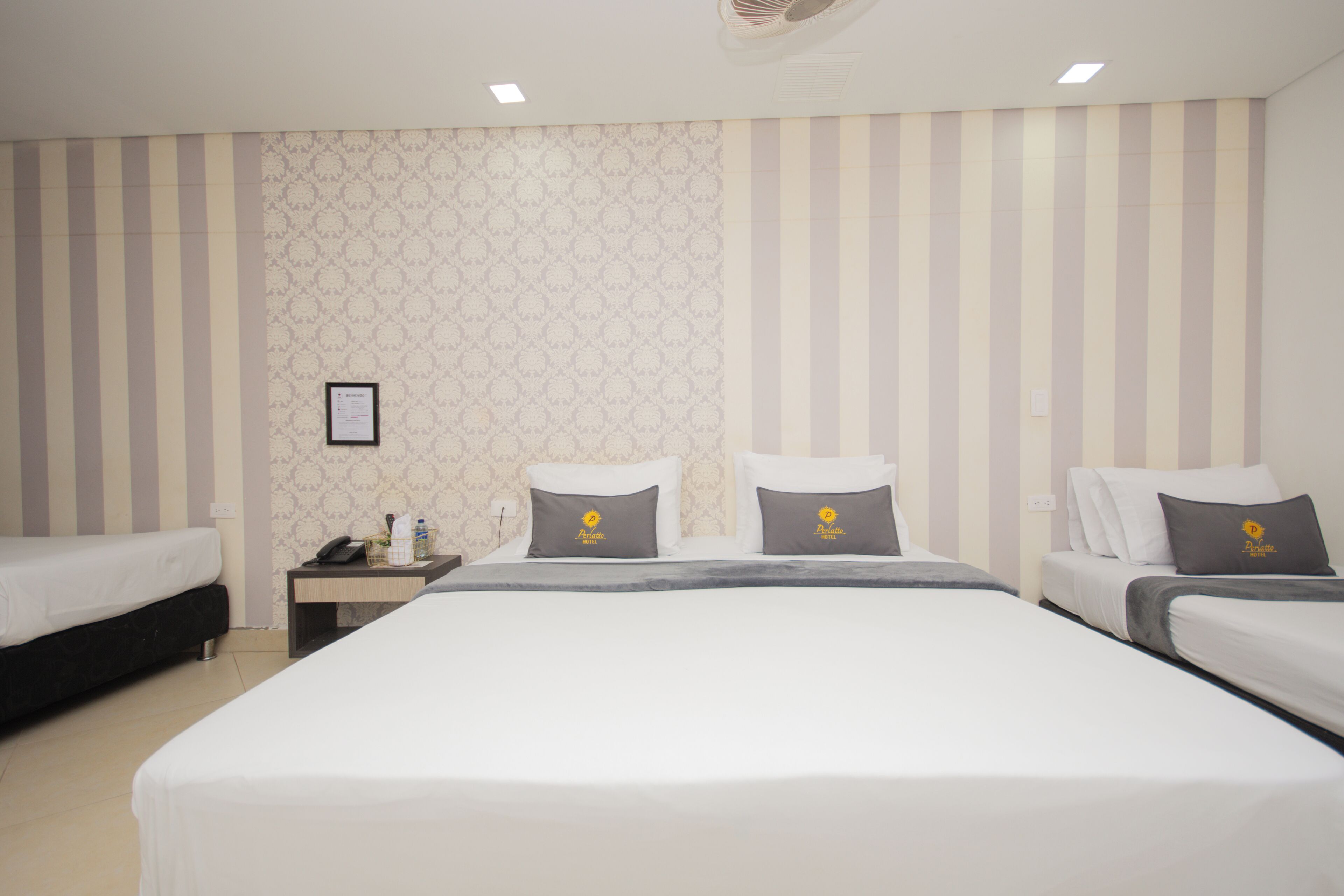 A hotel room with two single beds, a large bed, and a nightstand with a phone.