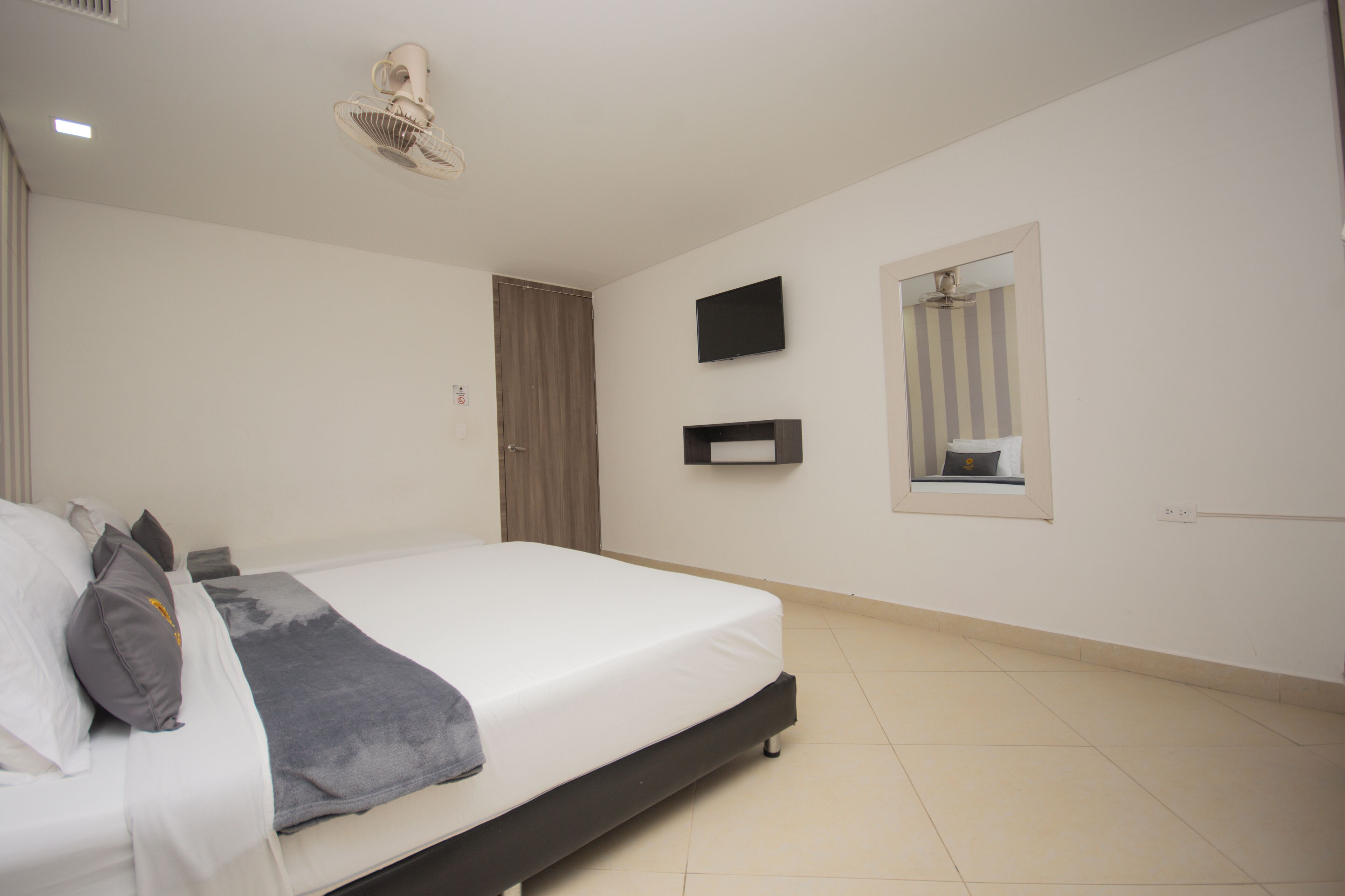 A bedroom with a bed, a TV mounted on the wall, and a mirror above the door.