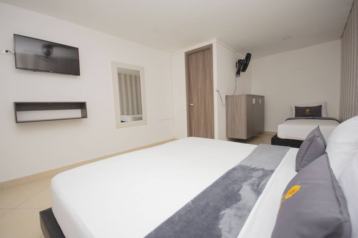 Quarto de hotel com cama grande, televisão na parede, guarda-roupa e uma janela pequena.