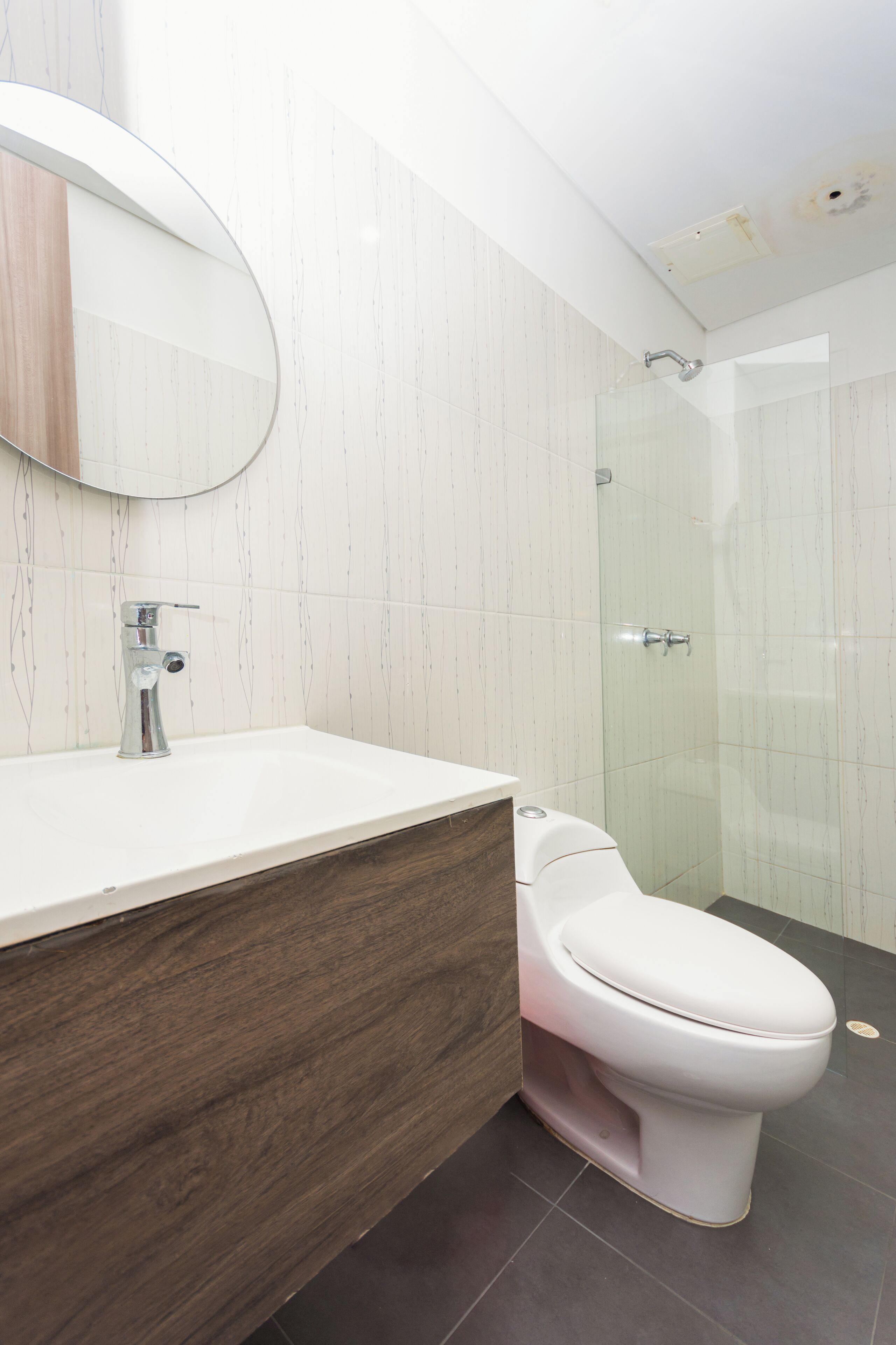 A modern bathroom with a white sink, a round mirror, a white toilet, and a glass shower enclosure.