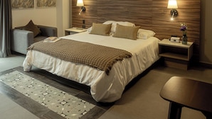 Une chambre d’hôtel moderne avec un grand lit, deux tables de chevet, une petite table, une chaise et un tapis décoratif.
