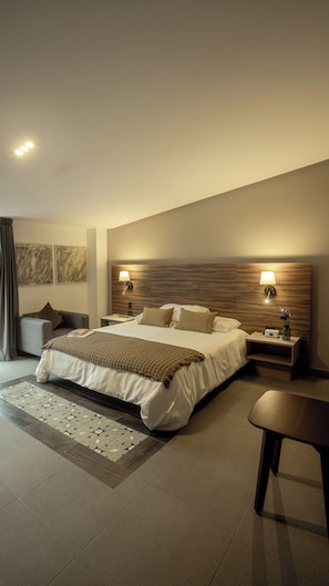 Una habitación de hotel moderna con una cama grande, dos mesitas de noche, un revistero, una silla y una alfombra decorativa.