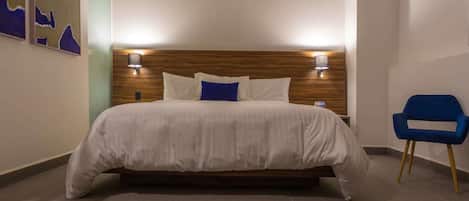 Habitación de hotel con una cama grande, dos lámparas de pared, un sillón azul y baldosas de suelo estampadas.