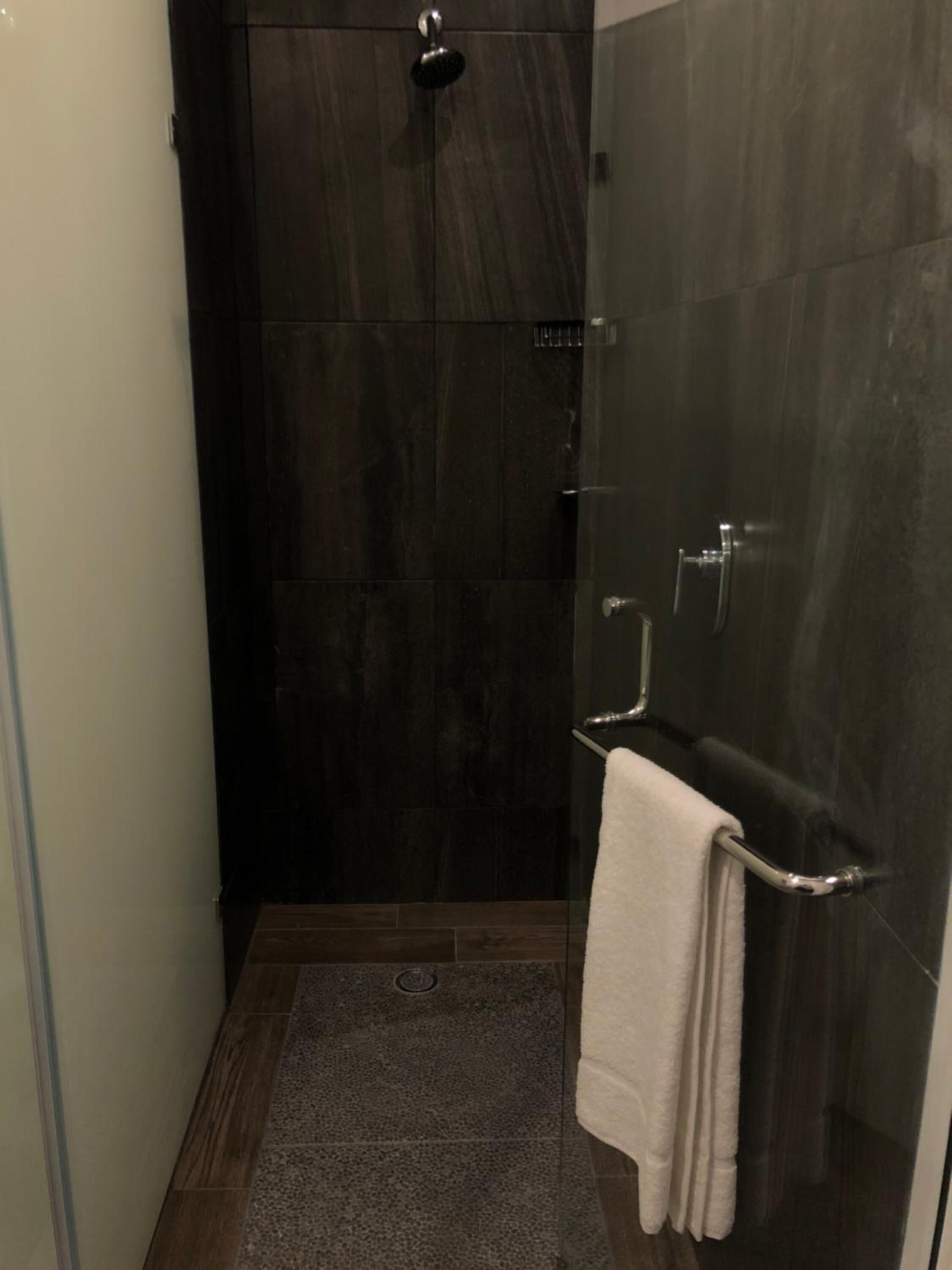 A small, dark-toned bathroom with a shower, a towel rack, and a glass door.