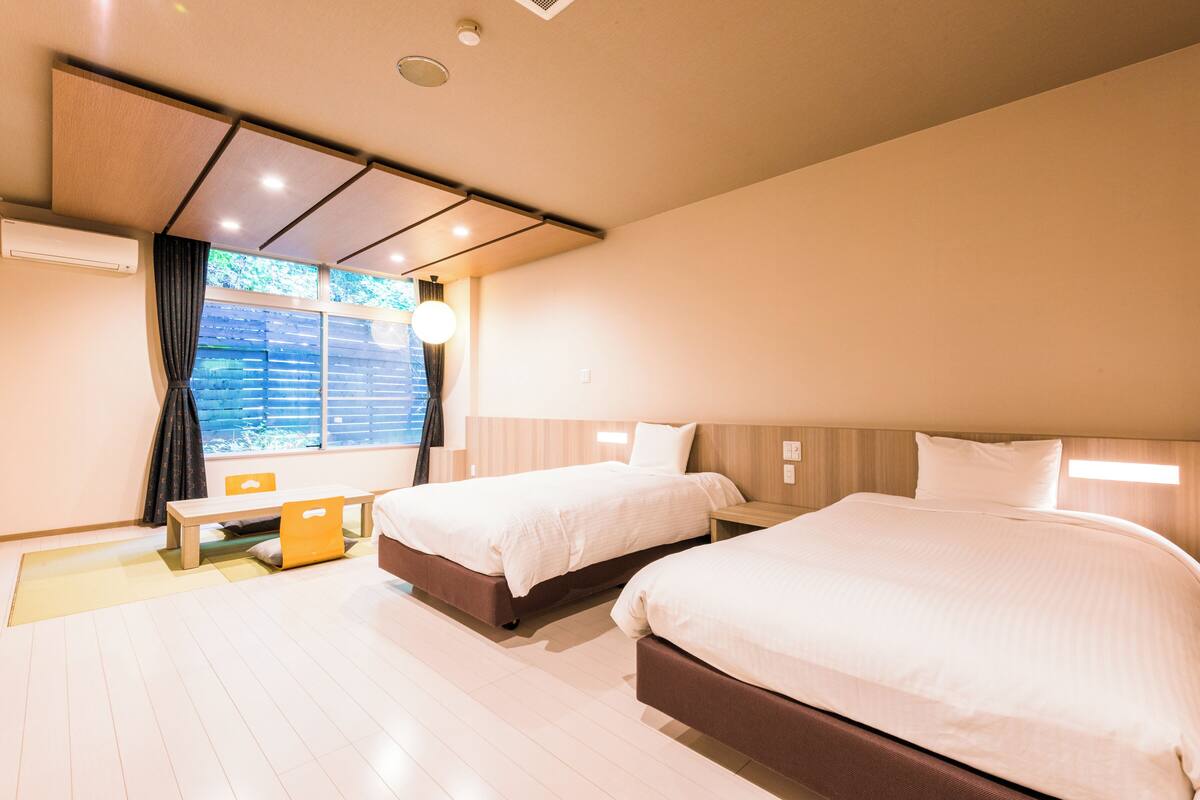 A hotel room with two beds, a small table, and a window with curtains.