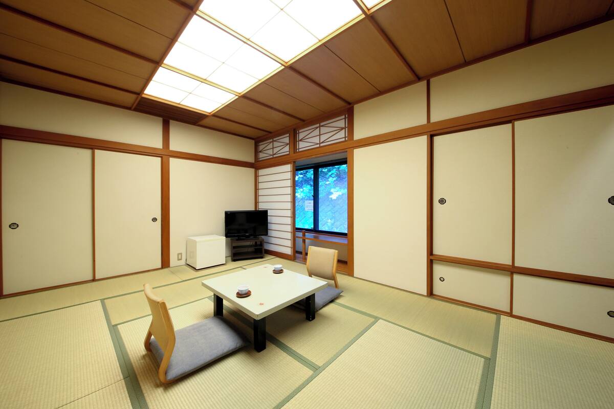 A traditional Japanese room with tatami flooring, a low table with cushions, a television, and sliding doors.