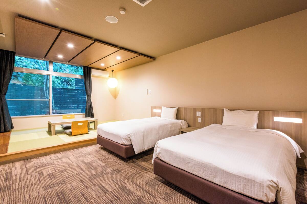 A hotel room with two beds, a desk, and a window with curtains.