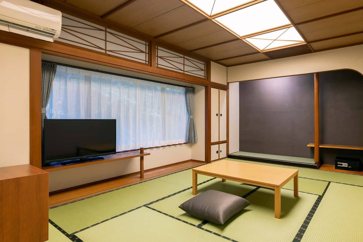 Une pièce de style japonais traditionnel, avec un sol recouvert de tatamis, un téléviseur, une porte coulissante et un ventilateur de plafond.