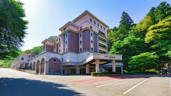 A multi-story hotel with a prominent entrance, a parking lot, and lush greenery surrounding the building. - Ooedo Onsen Monogatari Premium Ikaho (Shibukawa)