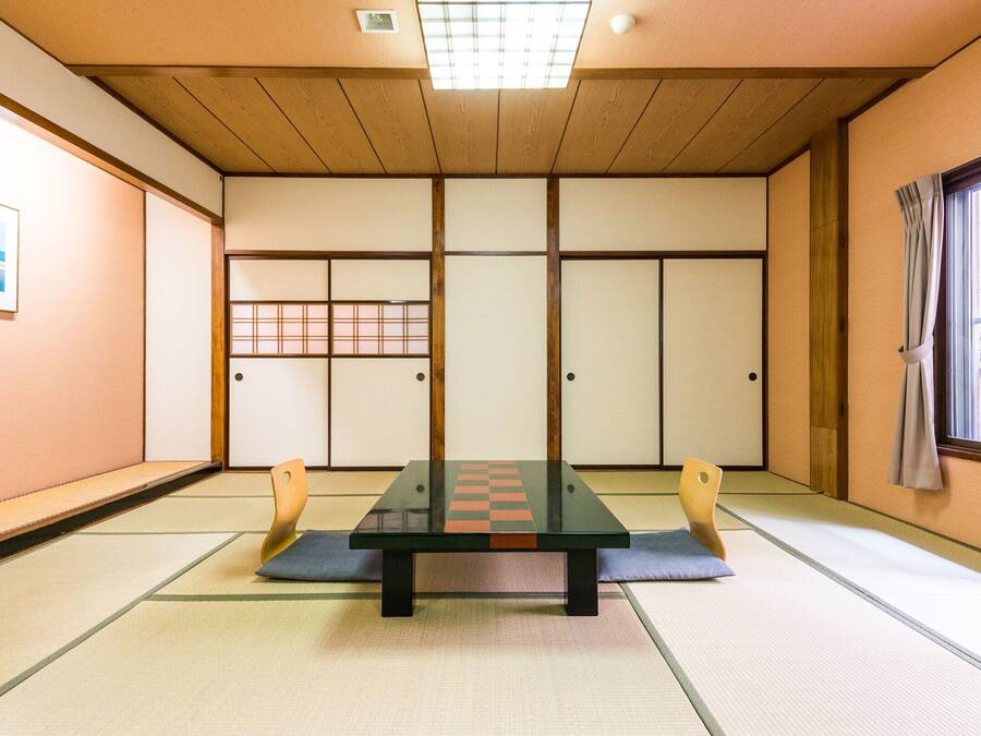 A tatami mat room with a low table, sliding doors, and a window with curtains.