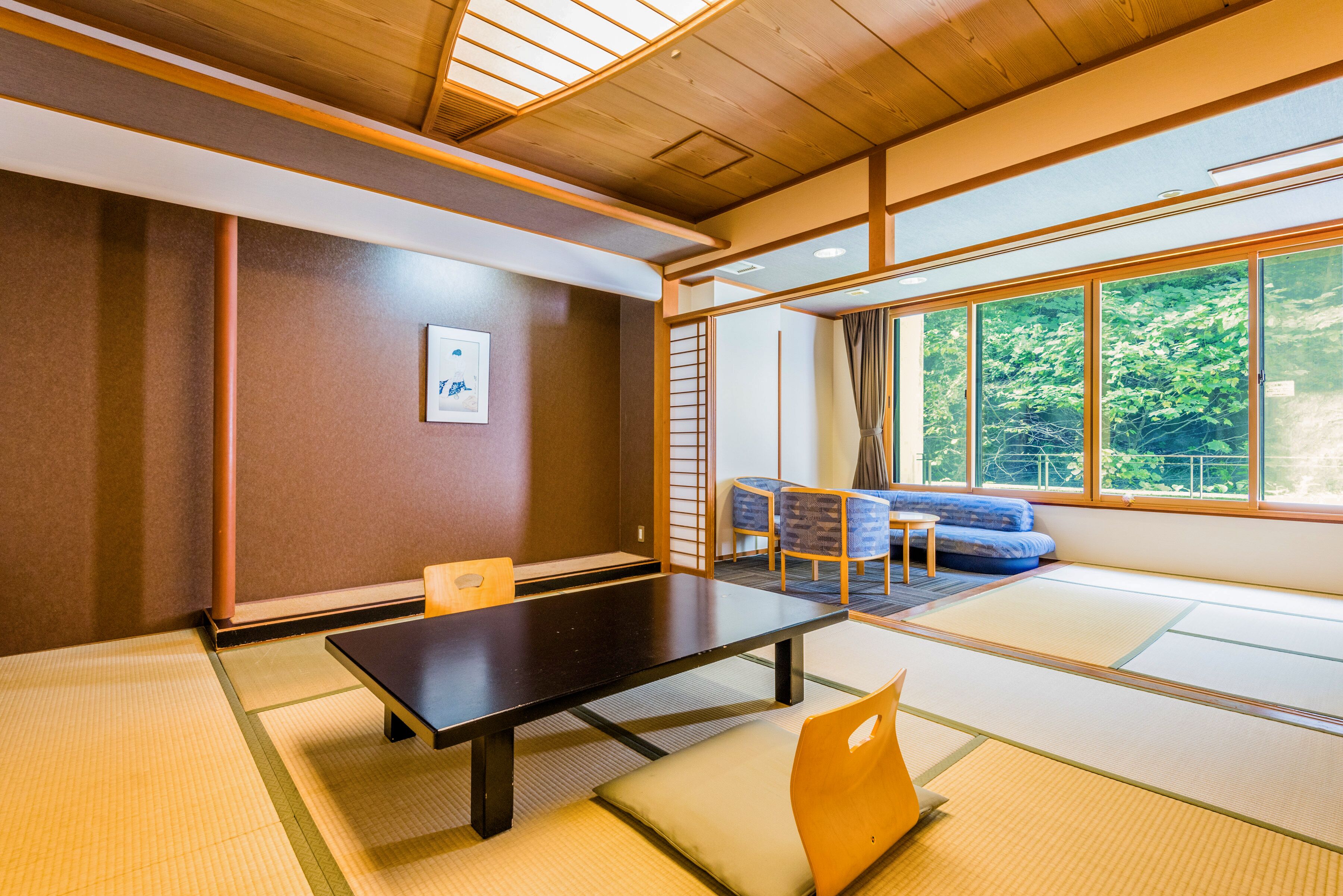 A traditional Japanese room with tatami flooring, a low table, and a view of greenery through large windows.