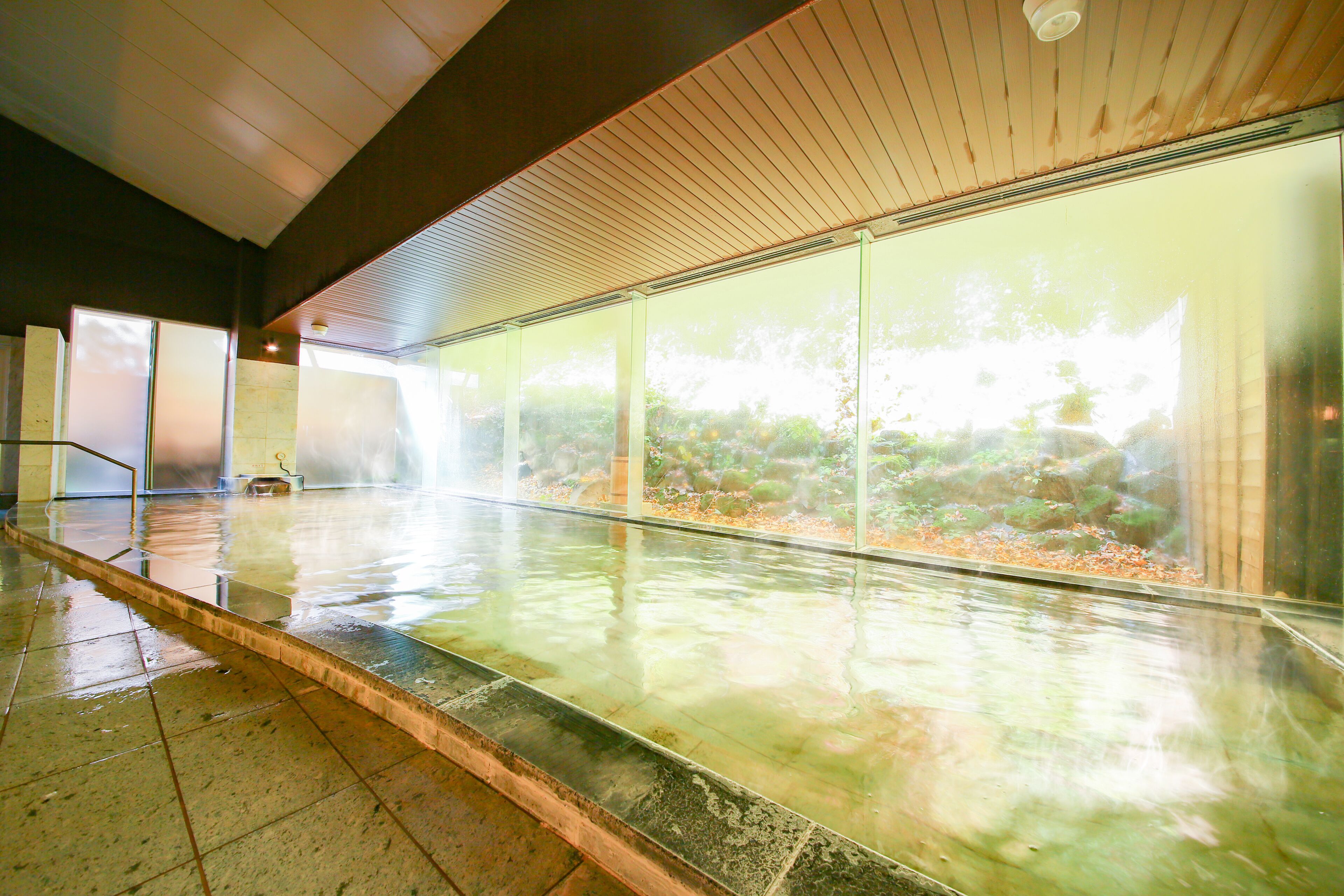 A spacious indoor area with a wet floor, large windows, and a wooden ceiling.