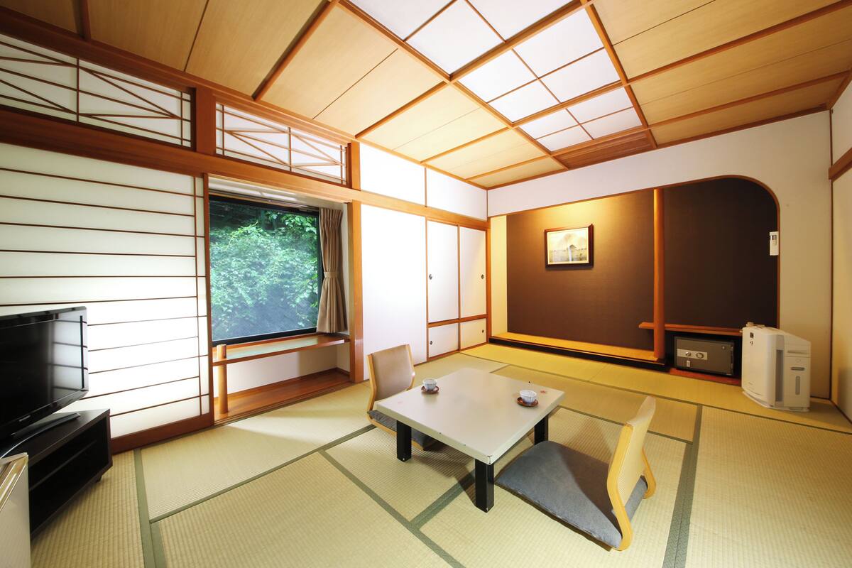 A traditional Japanese room with tatami flooring, a low table, chairs, a television, and a desk with a computer.