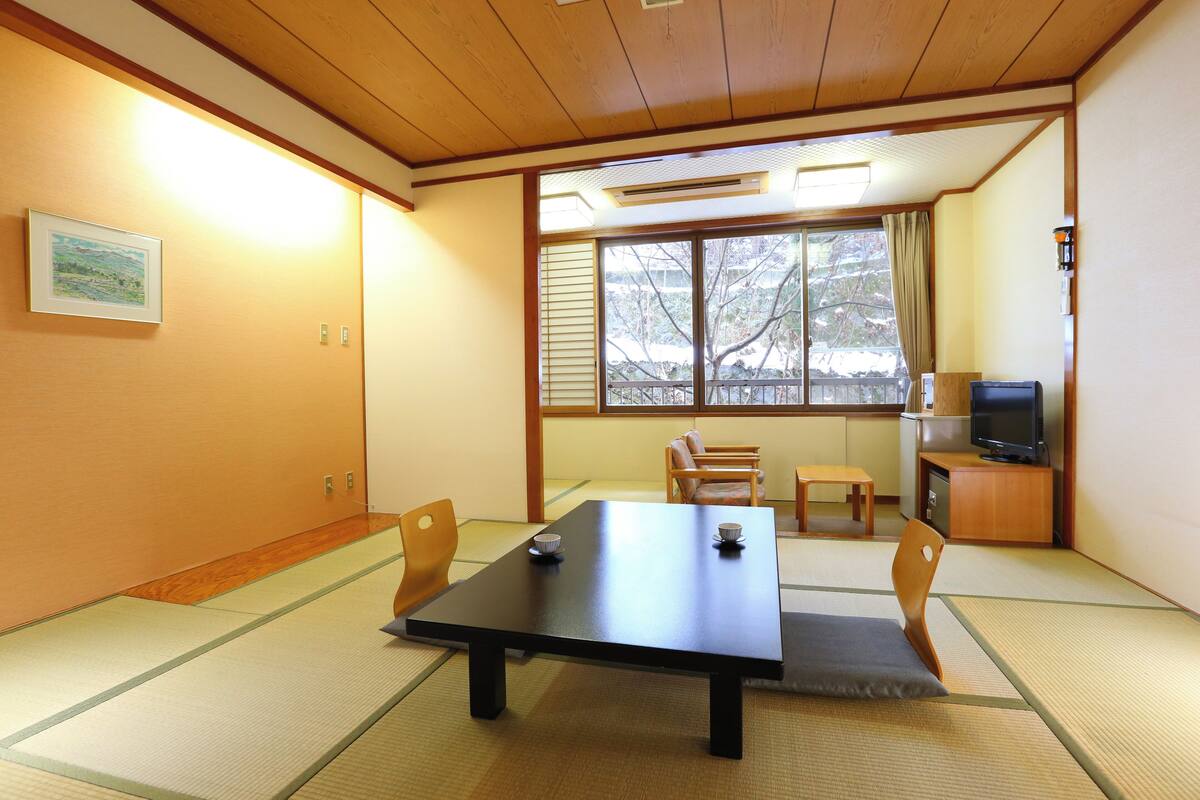 A traditional Japanese room with tatami flooring, a low table, and a television on a wooden cabinet.