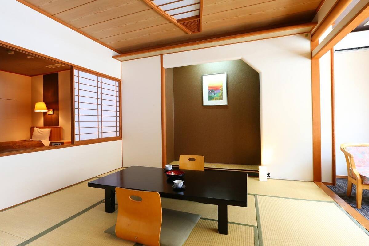 A traditional Japanese room with tatami flooring, a low table, a cushioned bench, and a sliding door.