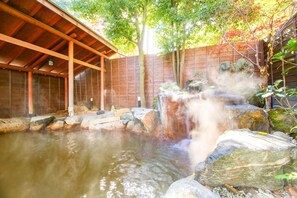 Un onsen japonés tradicional con estructura de madera, una piscina termal y una cascada.