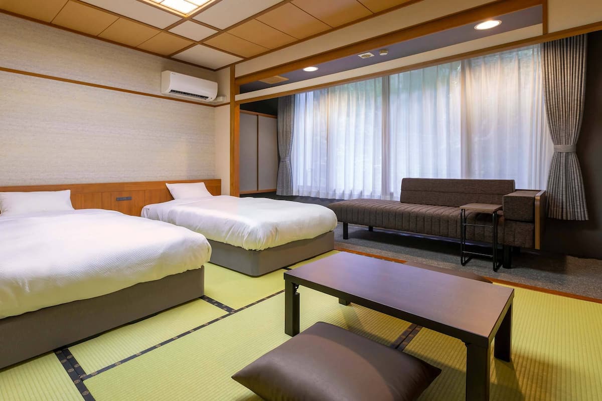 Une chambre d’hôtel avec deux lits, un canapé, une table et une grande fenêtre avec des rideaux.