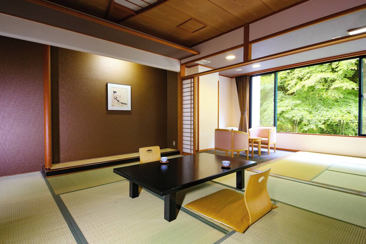 A traditional Japanese room with tatami flooring, a low table, and sliding doors leading to a view of greenery.