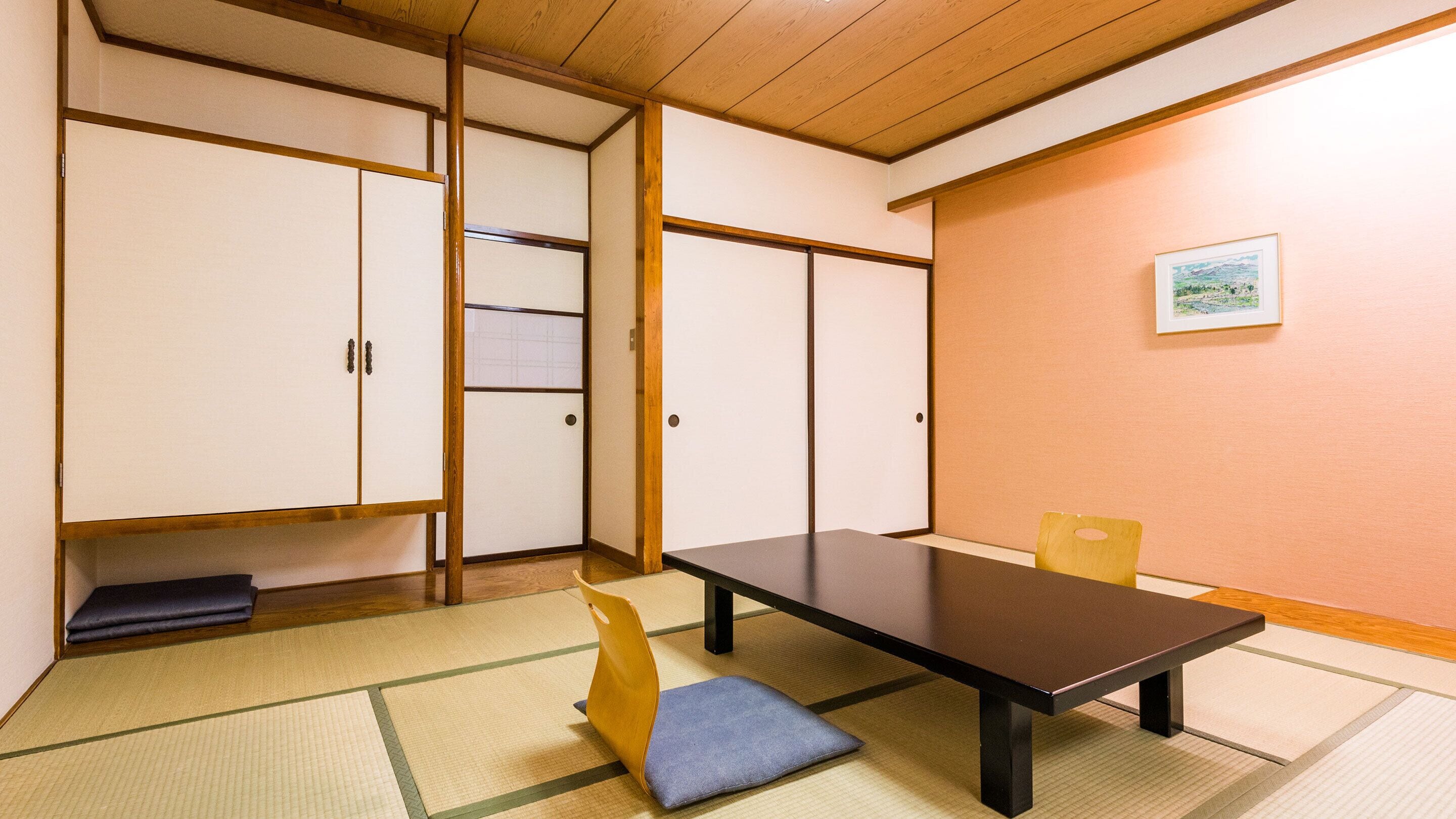 A traditional Japanese room with tatami flooring, a low table, a cushioned bench, and sliding doors.