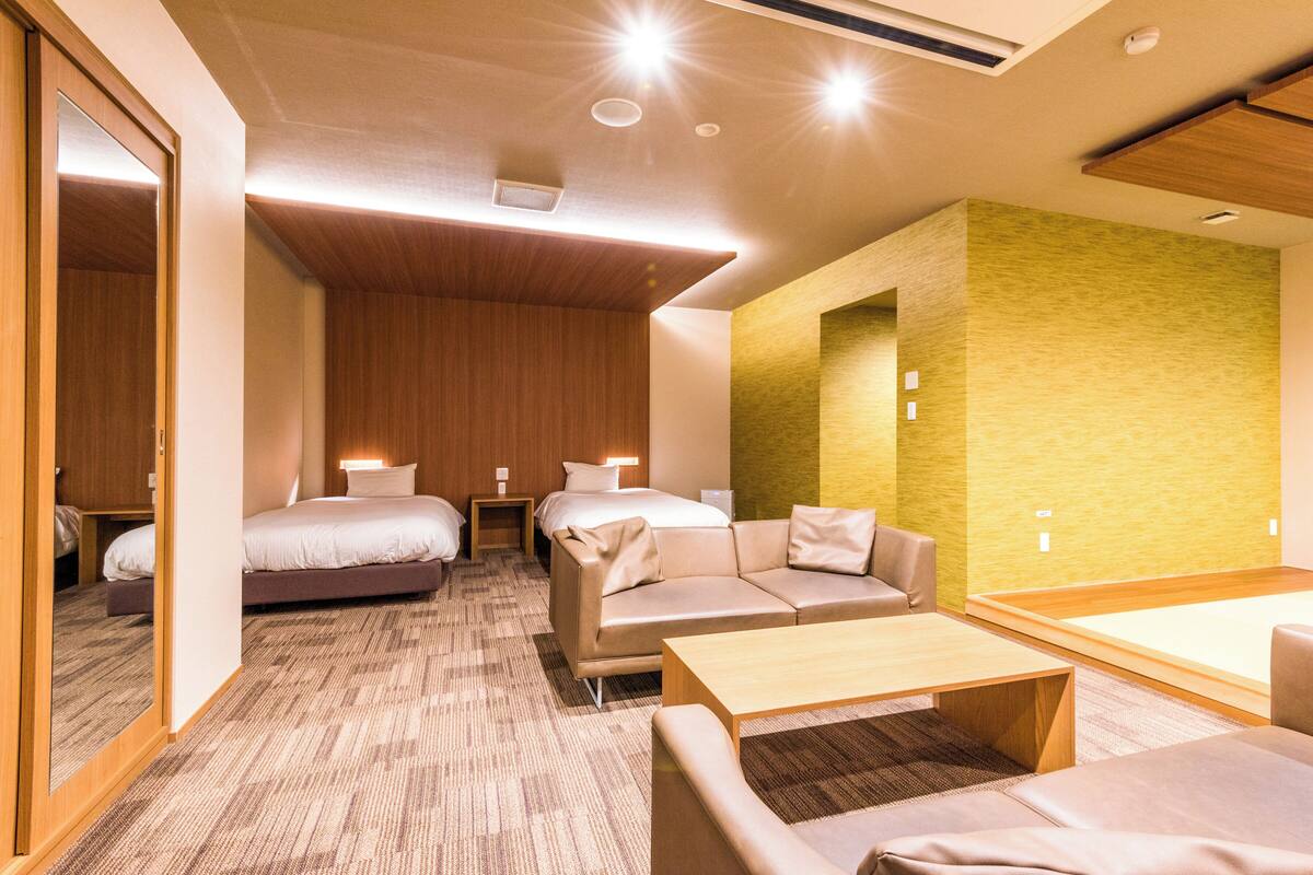 A hotel room with a bed, a sofa, a small table, and a mirror.
