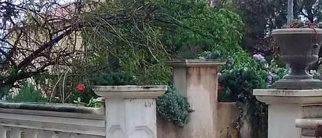 A set of stone steps leading up to a white balustrade, surrounded by greenery and a stone wall.
