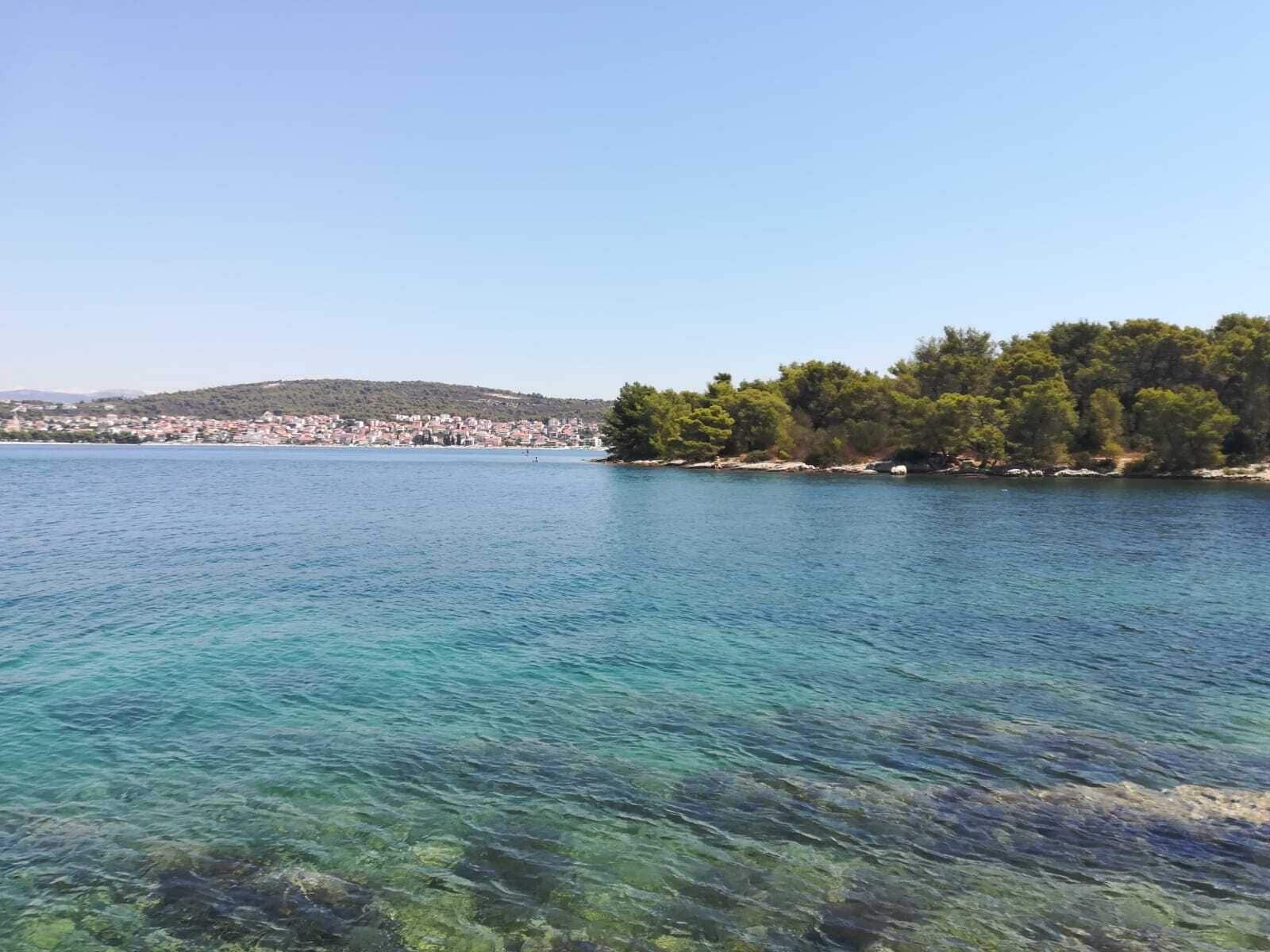 A coastal view with clear water, a distant town, and a forested area.