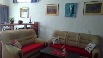 A living room with two beige sofas, a small table with a red placemat, and three framed artworks on the wall.
