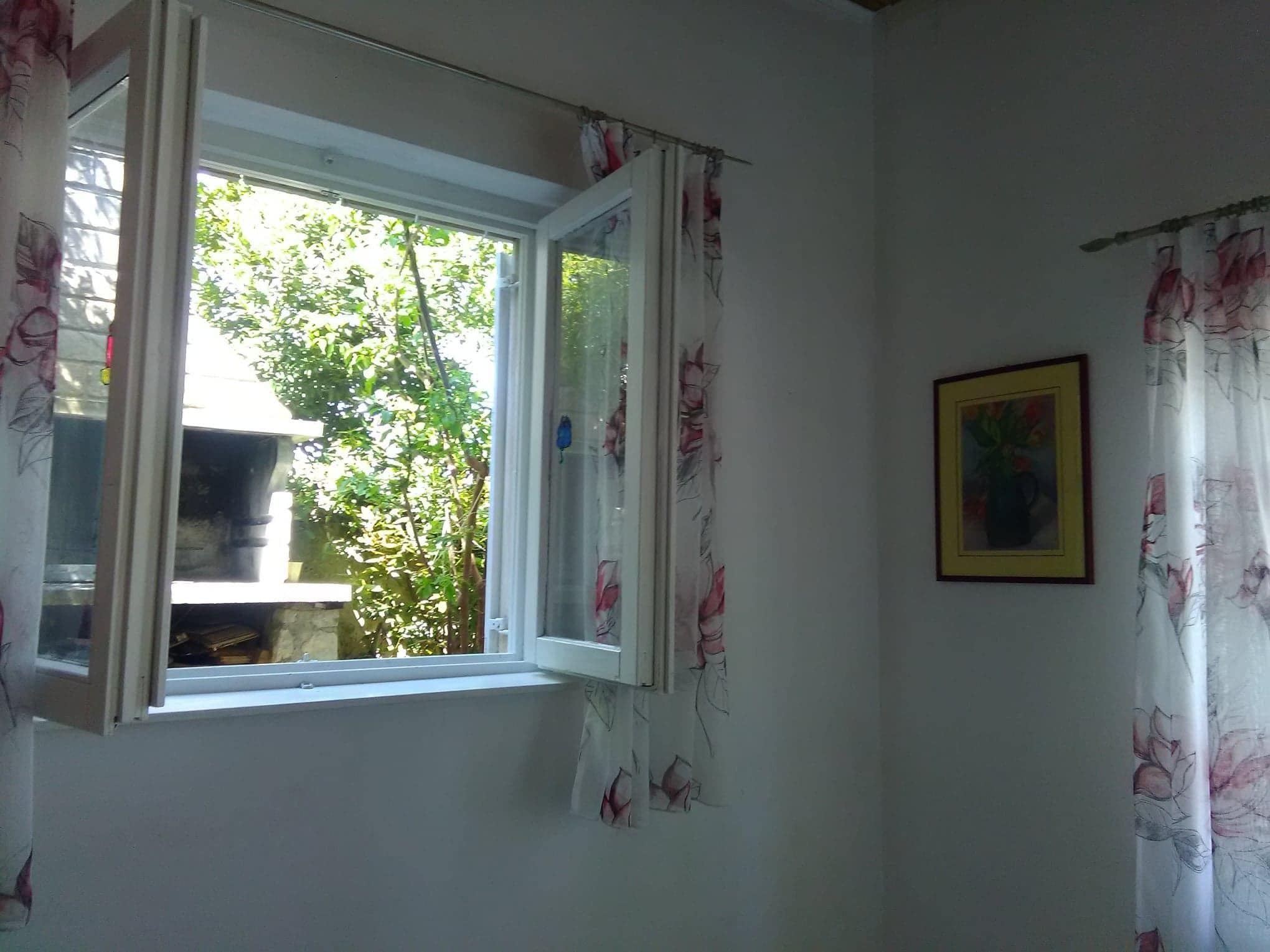 Una habitación con ventana, un cuadro enmarcado en la pared y cortinas con motivos florales.