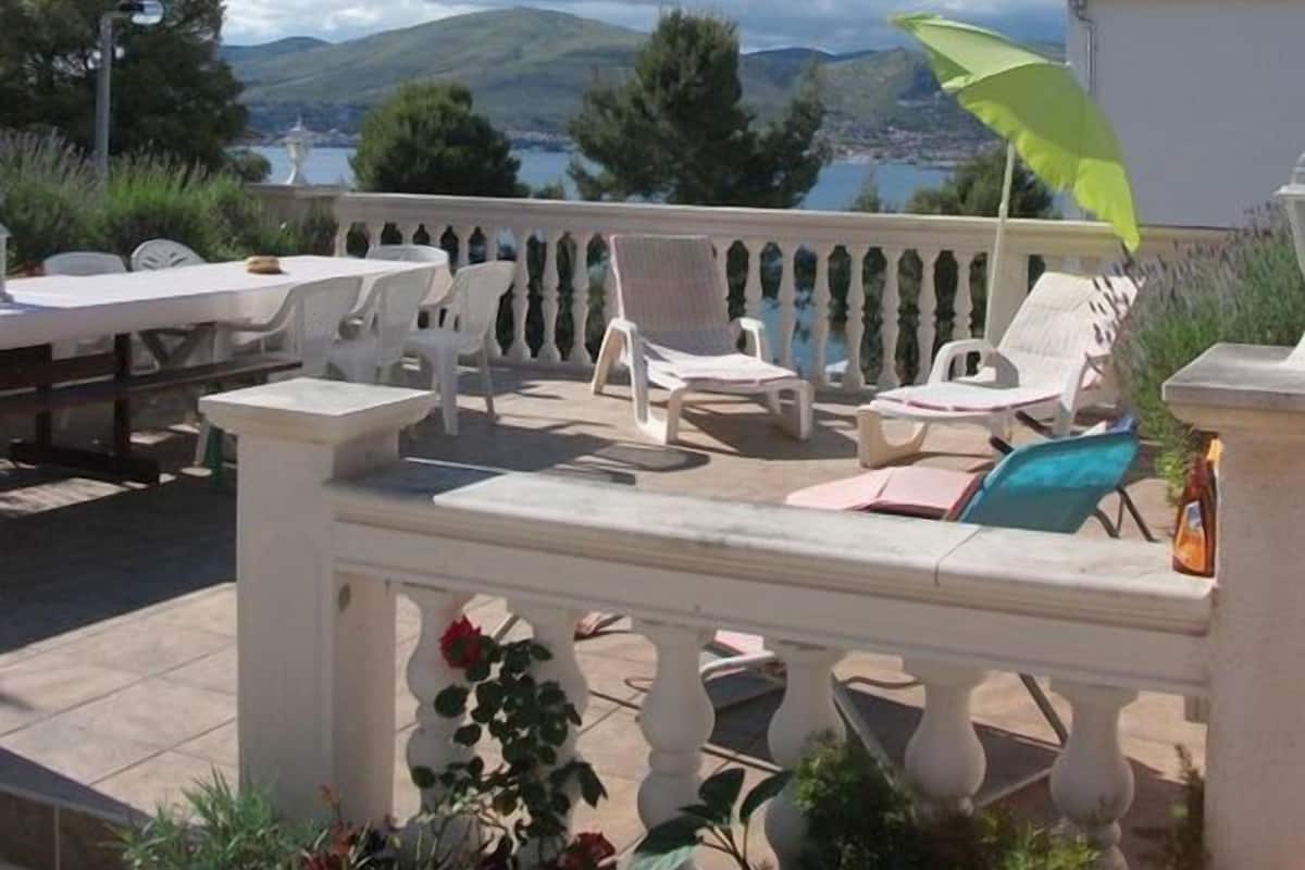 A terrace with outdoor seating, a view of the sea, and mountains in the background.