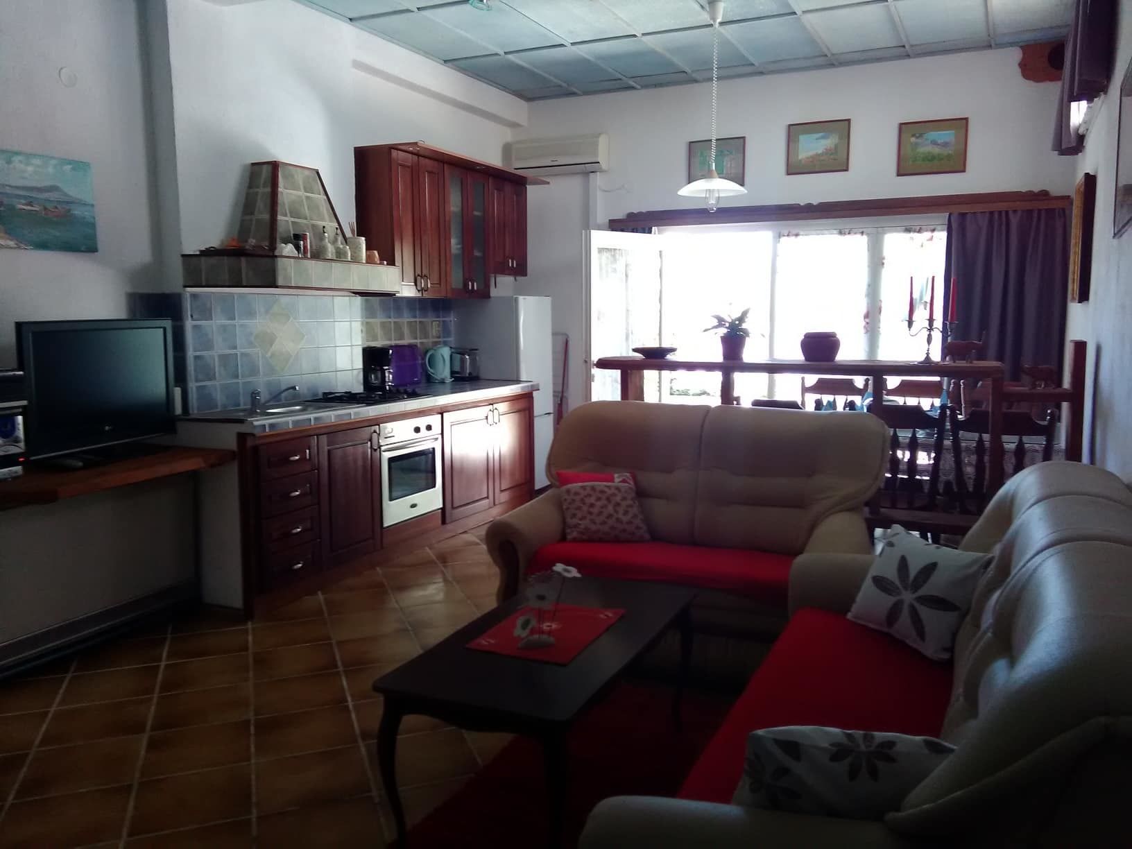 Un espacio habitable compacto con kitchenette, sofá, mesa de comedor y televisor.