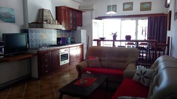 Un espacio habitable compacto con kitchenette, sofá, mesa de comedor y televisor.