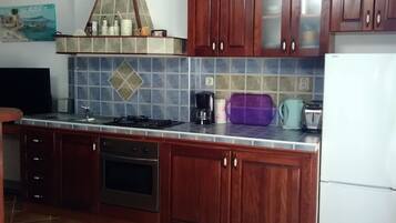 A kitchen with wooden cabinets, a tiled backsplash, a stove, a refrigerator, and a table with a lace tablecloth.
