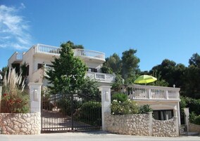 Un edificio de dos pisos con balcón, paredes de piedra y entrada con reja.