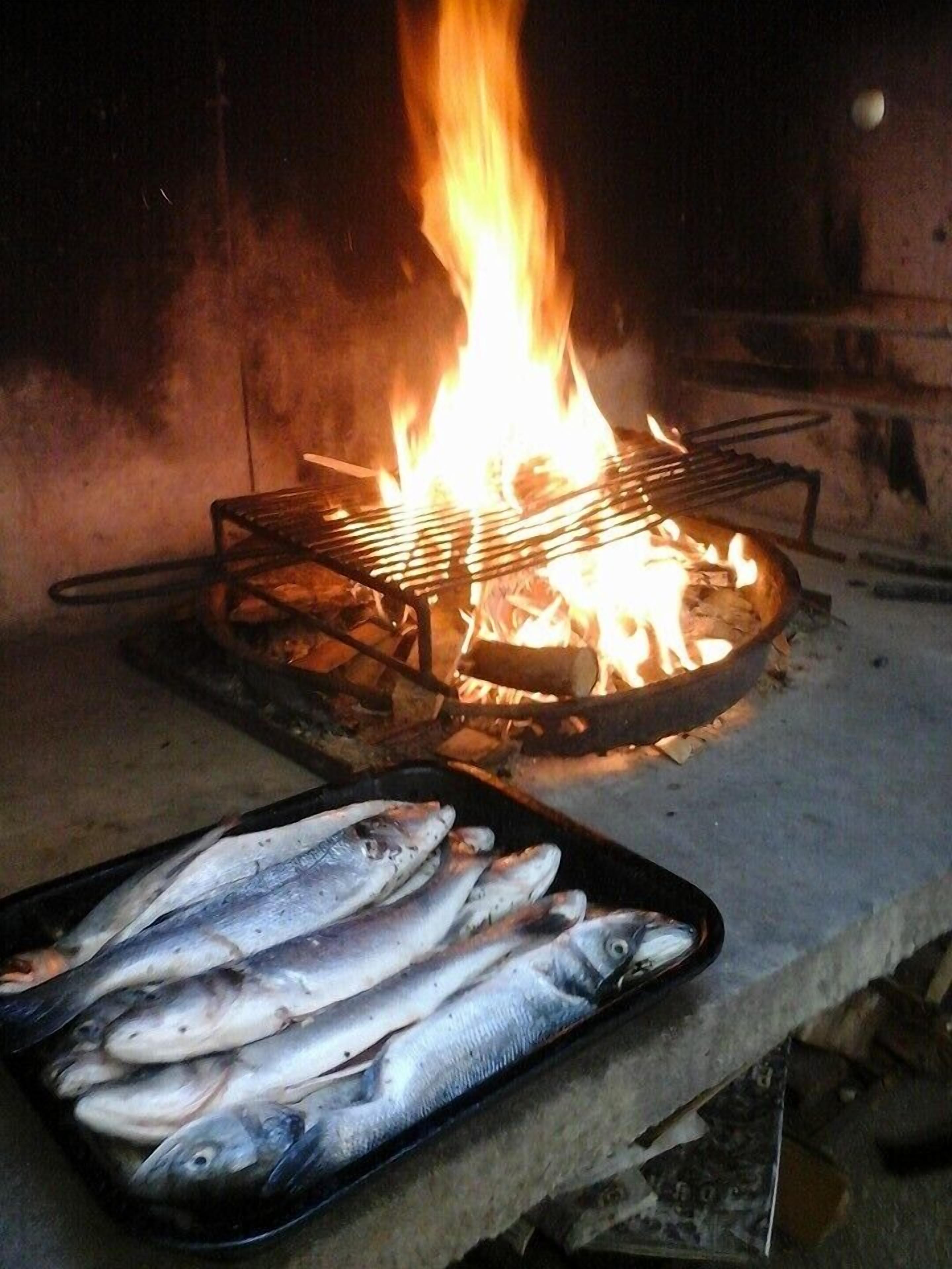 A grill with fish on a tray, a fire burning in the background, and a brick wall.