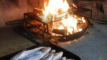 A grill with fish on a tray, a fire burning in the background, and a brick wall.