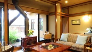 A living room with a wooden coffee table, sofa, and a large window with a view of greenery. - Okutsumagoi Onsen Hanaichi Hoshikawa Ryokan (Tsumagoi)