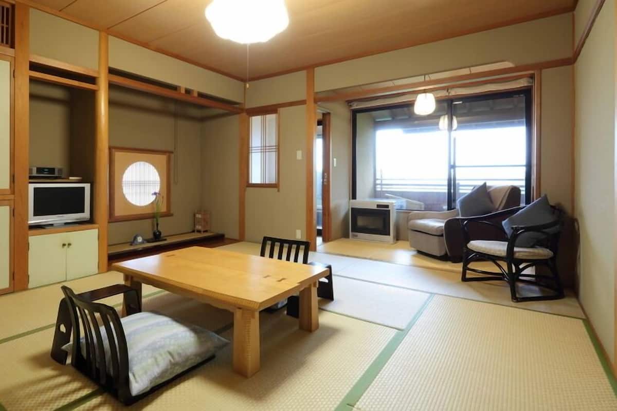 A traditional Japanese-style room with tatami flooring, a low table, a television, a sofa, and a chair.