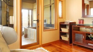 A room with a wooden floor, a sofa, a glass door leading outside, a wooden cabinet with a sink, and a mirror above the sink. - Okutsumagoi Onsen Hanaichi Hoshikawa Ryokan (Tsumagoi)