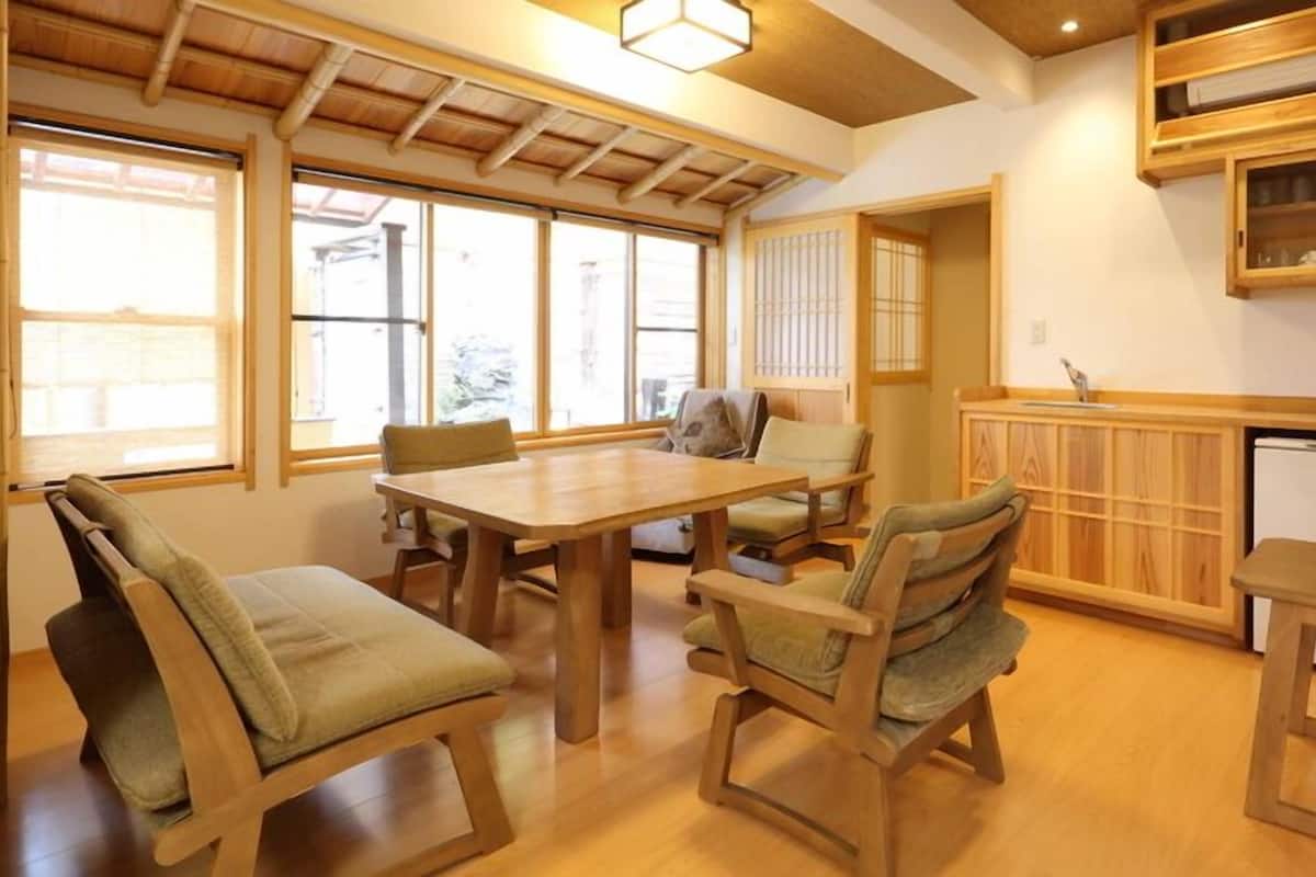 A traditional Japanese-style room with tatami mat flooring, a wooden dining table, and a kitchen area with a refrigerator and cabinets.