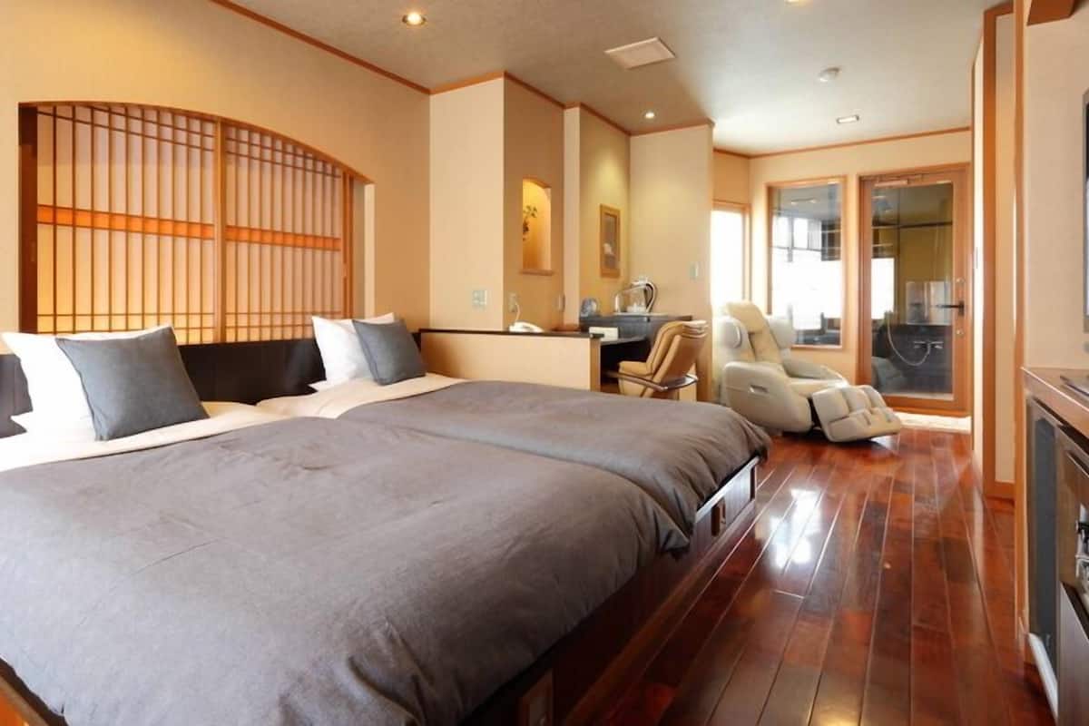 A hotel room with a large bed, a massage chair, a desk, and a TV.