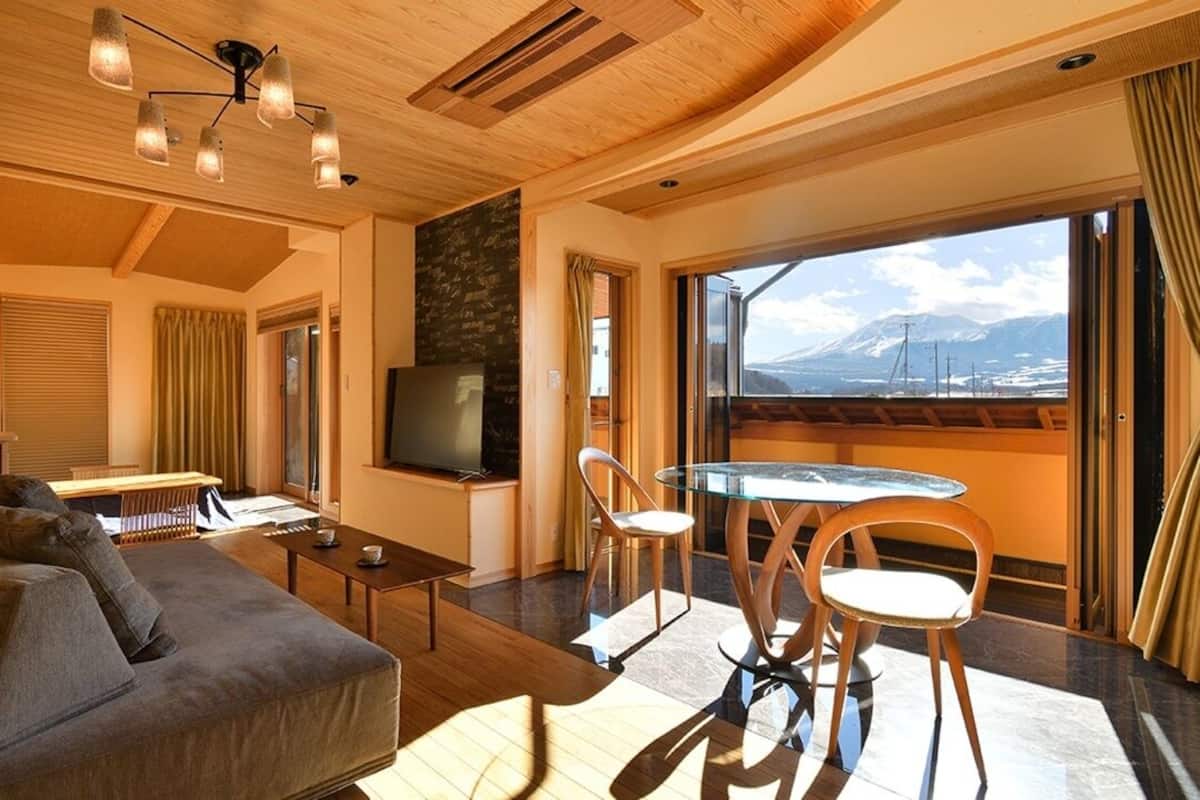 A modern living room with a sofa, a dining table with chairs, a TV, and a view of mountains through large windows.