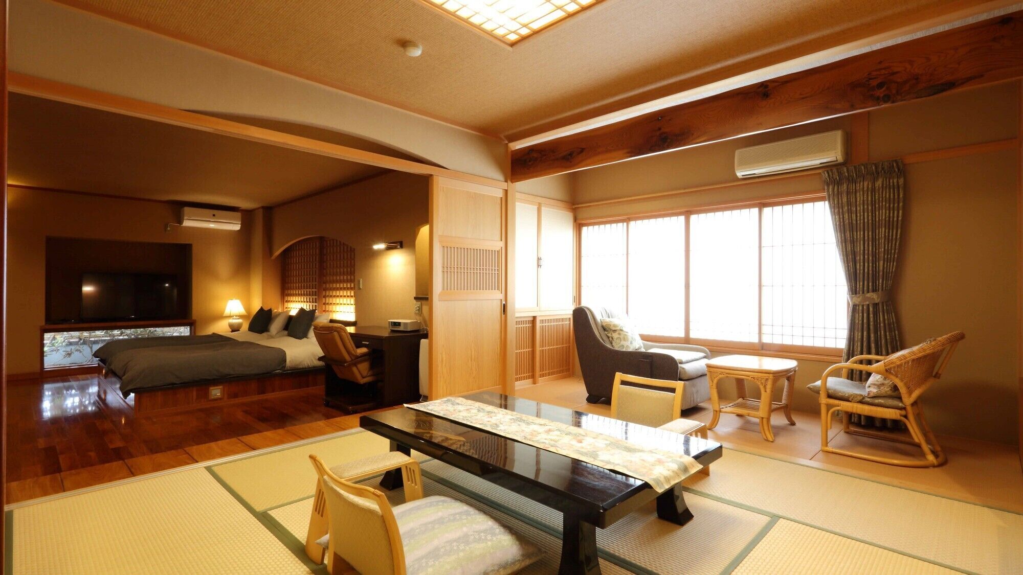 Ein traditioneller japanischer Raum mit Tatami-Boden, einem niedrigen Tisch, Stühlen, einem Bett und einem Fernseher.