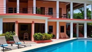 A two-story building with a swimming pool, outdoor seating, and a covered area with plants. - Coral House (Punta Gorda)