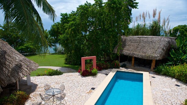 A swimming pool with stone tiles, a thatched-roof structure, and a glass table with chairs. - Coral House (Punta Gorda)
