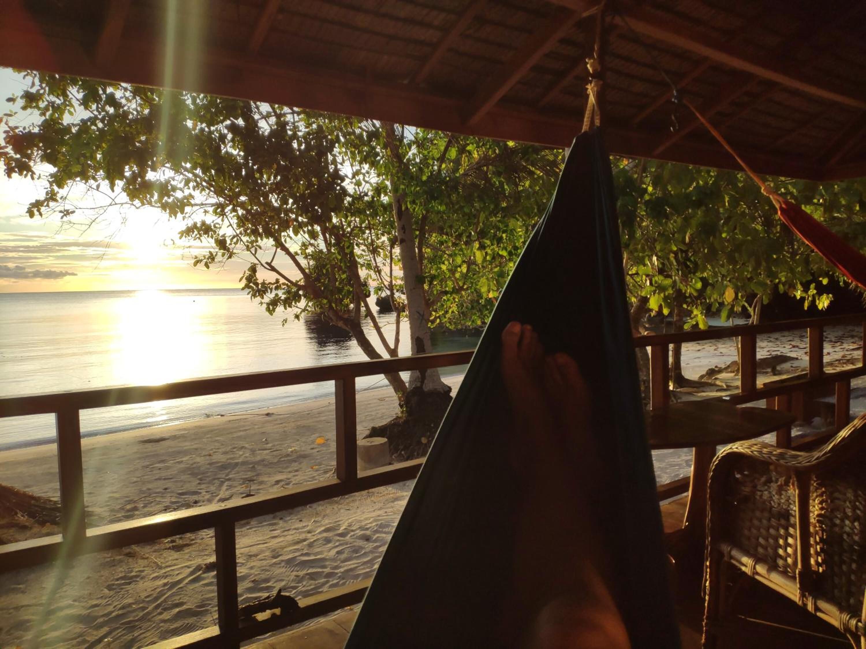 A hammock under a wooden structure with a view of the beach and ocean.