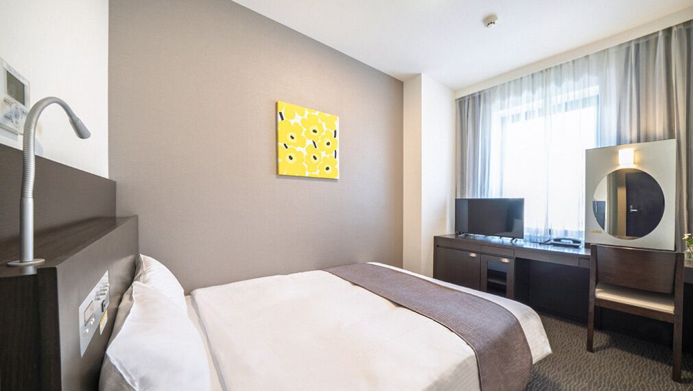 A hotel room with a bed, a desk, a chair, a TV, a mirror, and a window with curtains.