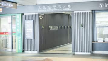 The entrance to Osaka Airterminal Hotel with a modern design, including a green ATM sign and a signboard with hotel information.