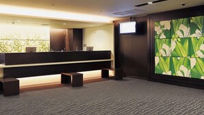 A reception area with a long counter, a television mounted on the wall, and a decorative panel with a floral pattern. - Osaka Airterminal Hotel (Toyonaka)