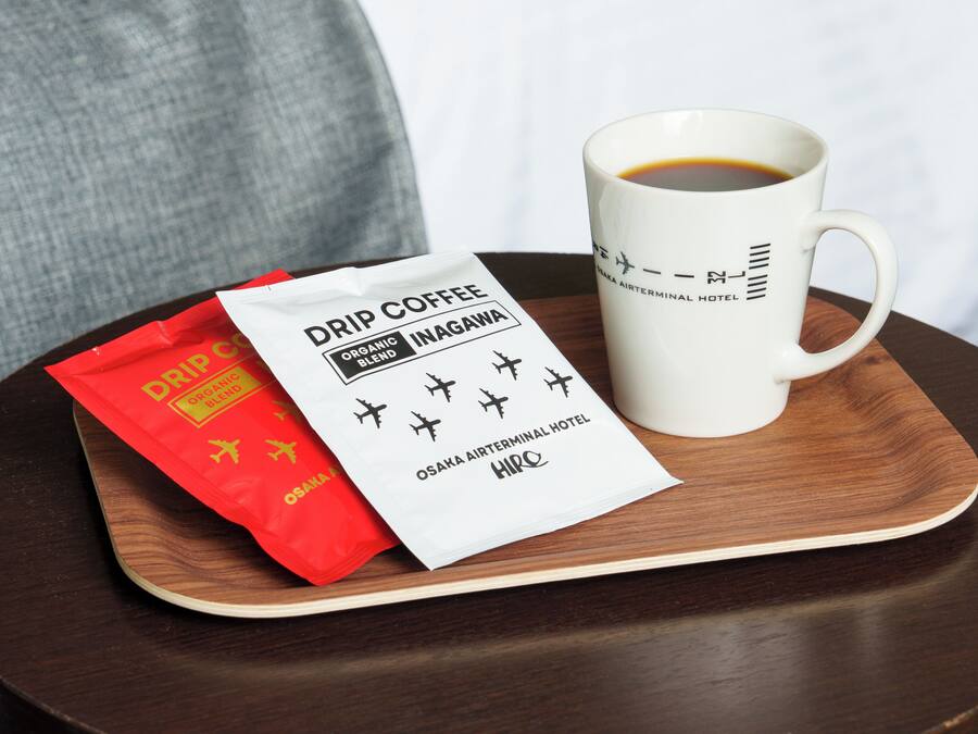A white mug with a logo, a red packet of drip coffee, and a white label on a wooden tray.